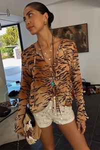 Tiger-print, brown sheer blouse with tie front; white textured shorts with circular accents; layered gold necklaces and clutch bag.