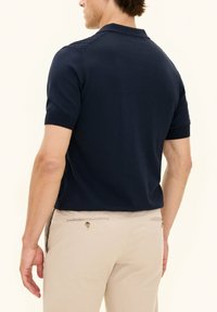 Mörkblå kortärmad polo med krage, med en texturerad bakdel och ribbade ärmslut. Matchas med beige byxor.