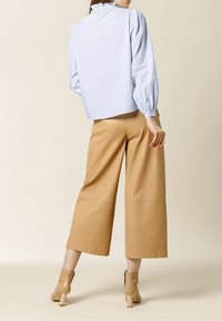 Blusa a righe blu chiaro con maniche a sbuffo e colletto arricciato, abbinata a pantaloni larghi beige e stivaletti beige con tacco a blocco.