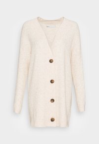 Vaaleanbeige neuletakki teksturoidusta kankaasta, jossa on V-kaula-aukko, pitkät hihat ja edessä viisi ruskeaa nappia.