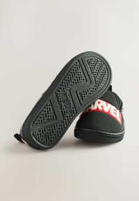 Sorte stof slip-on sko med rød "MARVEL" logo bånd, struktureret gummisul og en løkke ved hælen for nem påtagning.