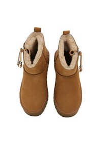 Para tanowych botków za kostkę z puszystym kremowym wykończeniem i bocznymi frędzlami, pokazana z góry na białym tle.