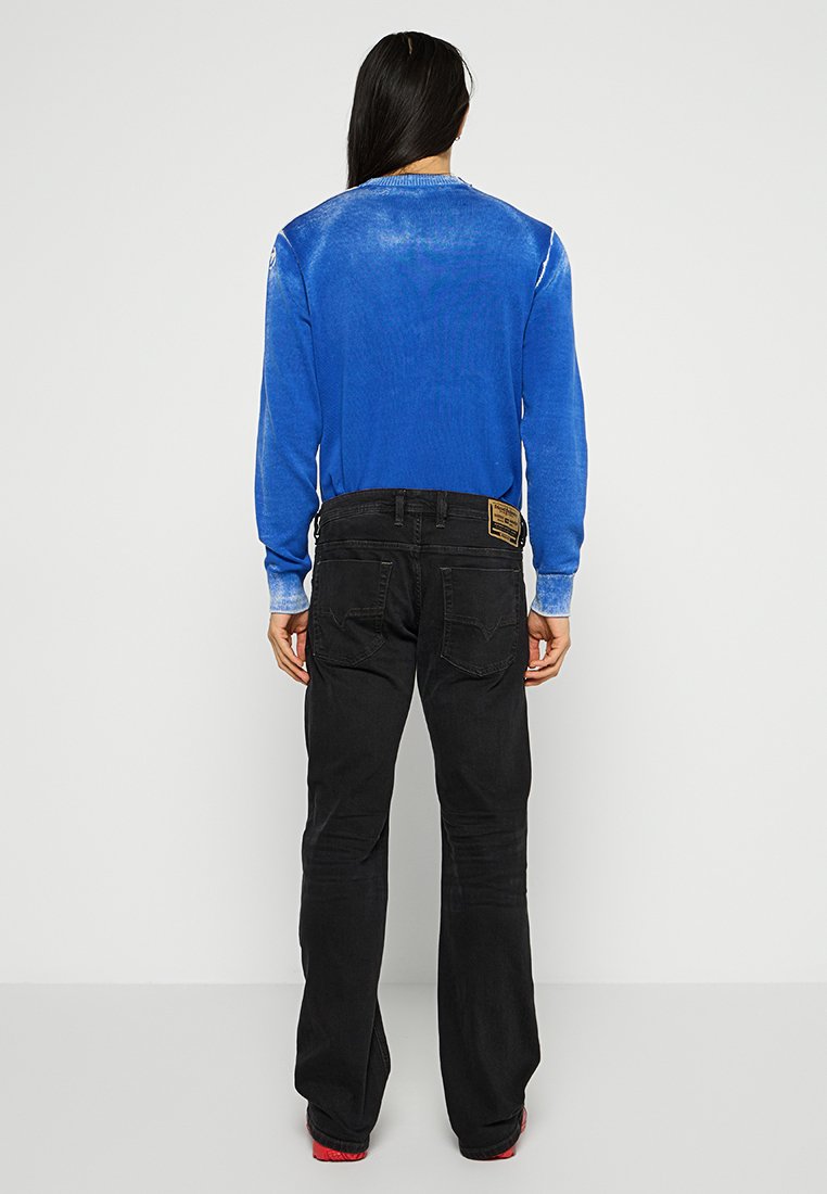 Pull en tricot bleu avec un dégradé plus clair aux ourlets, associé à un pantalon cargo noir avec des poches arrière et une étiquette sur la ceinture.