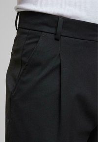 Pantalons noirs ajustés avec une taille plate, des poches latérales et une texture subtile. Le tissu semble lisse avec une coupe structurée.