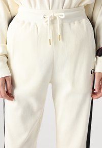 Weiße, gerippte Sweatpants mit elastischem Bund und Kordelzug, ausgestattet mit schwarzen Seitenstreifen und goldenen Akzenten an den Kordelenden.