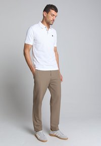Witte polo met een kraag en een klein logo, gecombineerd met lichtbruine broek en grijze sneakers met witte strepen. Eenvoudig ontwerp, geen patronen.