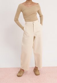 Beige väritetty pitkähihainen pusero olkapäät paljastavalla designilla, yhdistetty korkeavyötäröisiin, leveälahkeisiin kermaan vivahtaviin housuihin ja vaaleanruskeisiin puukenkään.