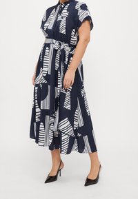 Vestido azul marino con rayas abstractas blancas, con mangas cortas, cuello y cintura ceñida con cinturón. La tela parece ligera y fluida.