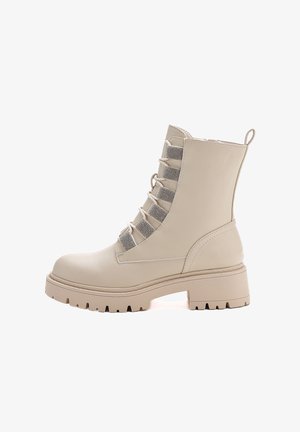 Stivale alla caviglia color crema con suola spessa, cerniera laterale e lacci decorativi su occhielli di tessuto luccicante.
