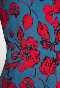 Robe fleurie en tissu bleu avec de grandes fleurs rouges et des contours noirs, mettant en valeur un design texturé avec des motifs vibrants.