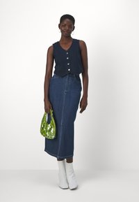 Jūros laivyboje trumpas viršus su knopkėmis, aukšto liemens džinsiniai sijonai, baltos aukštakulnės batus. Žalia blizganti rankinė suteikia kontrastą. Sklandus džinsinio audinio paviršius.