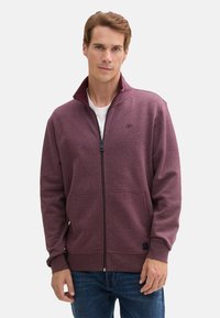 Giacca zip-up bordeaux realizzata in materiale morbido, con un alto colletto, due tasche anteriori e un logo sul lato sinistro del petto.
