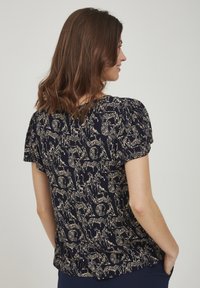 Blusa navy a maniche corte con un motivo animale beige ripetuto, dotata di dettagli arricciati sulle spalle e una vestibilità comoda.