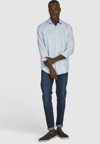 Lichtblauw overhemd met knopen, lange mouwen, gedragen met donkerblauwe jeans en marineblauwe instappers. Casual, aansluitend ontwerp met opgerolde mouwen.