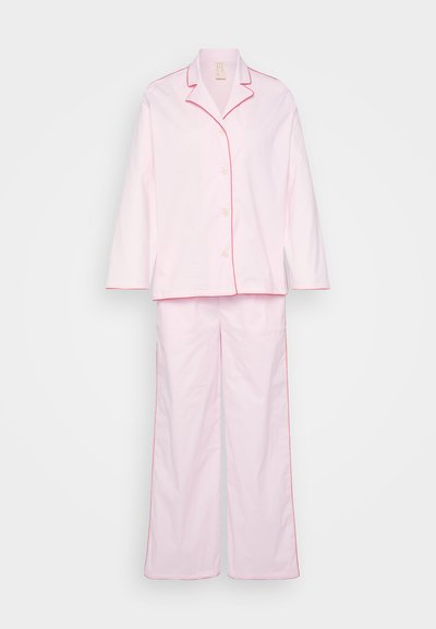 Ροζ πυτζάμα από μαλακό ύφασμα, με μακριά μανίκια και παντελόνι με αντίθετη κόκκινη ταινία κατά μήκος των άκρων. Κουμπωτή μπροστινή πλευρά από πάνω.