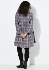 Abito a quadri grigi con accenti rosa e neri, vestibilità ampia, maniche lunghe e dettagli annodati in vita, abbinato a leggings neri e stivaletti.