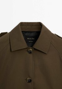 Ruskea napitettu takki, jossa on muotoiltu kaulus ja hartiapaikat, näkyy Maximo Dutti -merkkilogo kauluksen sisällä.