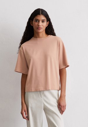 Short-sleeve, blush pink t-shirt made of soft cotton, featuring a round neck and a relaxed fit with a straight hem. Paired with light-colored pants.