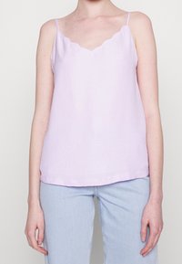 Levandulový top bez rukávů s vlnkovým výstřihem, vyrobený z texturované látky. Rovný lem a tenké nastavitelné ramínka. V kombinaci s světle modrými džíny.