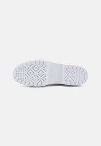 Semelle de sneaker en caoutchouc blanc avec un motif texturé. Présente des rainures et des formes de diamant surélevées pour l'adhérence. "CONVERSE" embossé au centre.