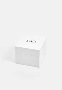 Balta kvadratinė dėžutė su matinio paviršiaus apdaila. Ant dangčio yra juodas logotipas su užrašu "FURLA" ir "SINCE 1927 / ITALY". Paprastas, švarus dizainas.