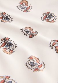 Tissu blanc avec des motifs floraux espacés de manière uniforme en bleu, orange et marron, avec des feuilles et des pétales stylisés.