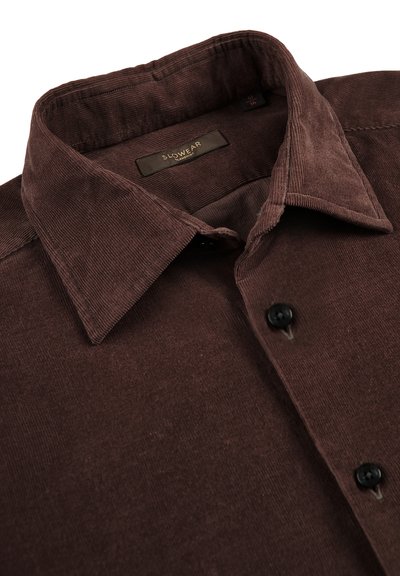 Bruine corduroy overhemd met puntige kraag, zwarte knopen en een zichtbare merklabel "Slowear" binnen de halslijn.