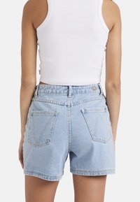 Helles blaues Denim-Shorts mit hoher Taille, zwei Gesäßtaschen und gelben Nähten. Glatte Textur mit lockerer Passform.