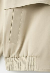 Tissu beige en gros plan montrant une poche cousue et un détail d'ourlet élastiqué sur un vêtement.