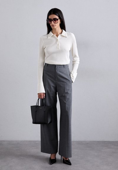 Haut à manches longues blanc côtelé, pantalon large gris, sac à main noir et escarpins noirs à bout pointu. De grandes lunettes de soleil carrées finalisent le look.