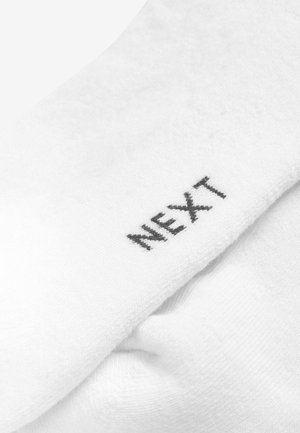 Hvid sok med blød tekstur; har en sort "NEXT"-logo broderet nær den øverste kant. Enkelt design, standardlængde.
