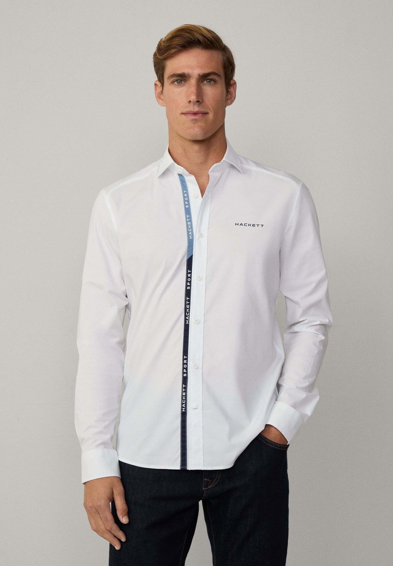Witte overhem shirt met een contrasterende blauwe zijpaneel met de tekst "HACKETT SPORT". Lange mouwen en een klassieke kraagontwerp.