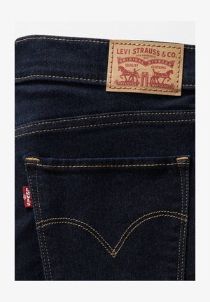 Dark blue denim jeans with a leather patch at the waistband detailing the brand. Features yellow stitching and a red tab on the back pocket.