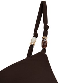 Tmavohnedý látkový remienok s dvoma uviazanými sekciami, ozdobený jednou bielou a jednou hnedou korálkou oddelenou zlatými krúžkami.
