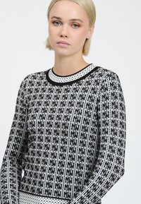 Maglione in bianco e nero con un motivo geometrico, scollo rotondo e tessuto textured con maniche lunghe.