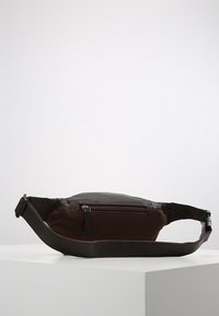 Braune Stoff- und Lederbauchtasche mit einer Vorderseite mit Reißverschluss, verstellbarem Gurt und flacher Form, geeignet für den alltäglichen Gebrauch.
