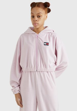 Sudadera con cremallera de color rosa claro y corte holgado, que cuenta con un bolsillo tipo canguro y puños elásticos. Incluye un pequeño logo de marca en el pecho.