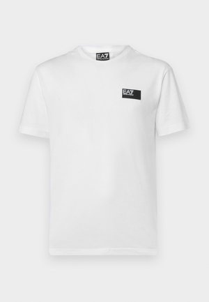 T-shirt bianca in cotone con maniche corte, collo rotondo a coste e una piccola etichetta nera rettangolare sul lato sinistro del petto.