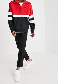Nike halvdraget sweatshirt i röd, vit och svart med djärva ränder, i kombination med svarta byxor och vita sneakers. Slät tygtextur.