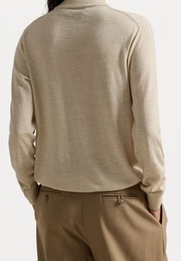 Pull-over beige en tricot avec manches longues et col. Présente une texture lisse. Associé à un pantalon marron sur mesure, soulignant les détails des poches.