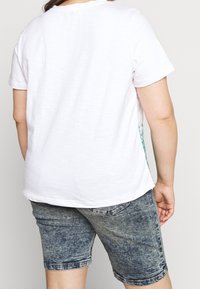 Valkoinen lyhythihainen t-paita pyöreällä pääntiellä, yhdistetty vaaleansinisiin denimhousuihin. Ei näkyviä kuvioita tai logoja.