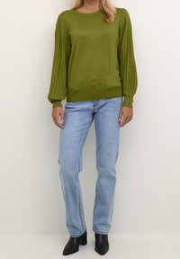 Maglione a maglia verde oliva con maniche a palloncino a coste, scollo rotondo, abbinato a jeans azzurri chiari e stivaletti neri con tacco.
