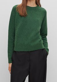 Dark green knitted sweater with a round neckline and ribbed cuffs. Textured fabric, slightly loose fit, paired with black wide-leg trousers.