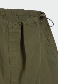 Pantalons olive drab avec taille élastique, dotés d'un cordon de serrage et d'un tissu doux et texturé, avec des plis sur le devant et des détails de couture.