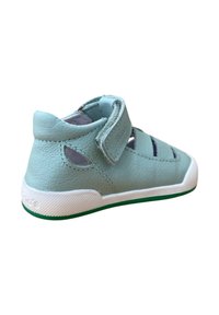 Zapato de cuero azul claro con un talón alto, correa ajustable, lados abiertos, suela blanca y acento verde. Acabado texturizado, diseño moderno.