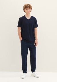 Tricou bleu marin cu decolteu în V din material moale, asociat cu pantaloni închiși la culoare și adidași albi. Design simplu, cu mâneci scurte și o croială lejeră.
