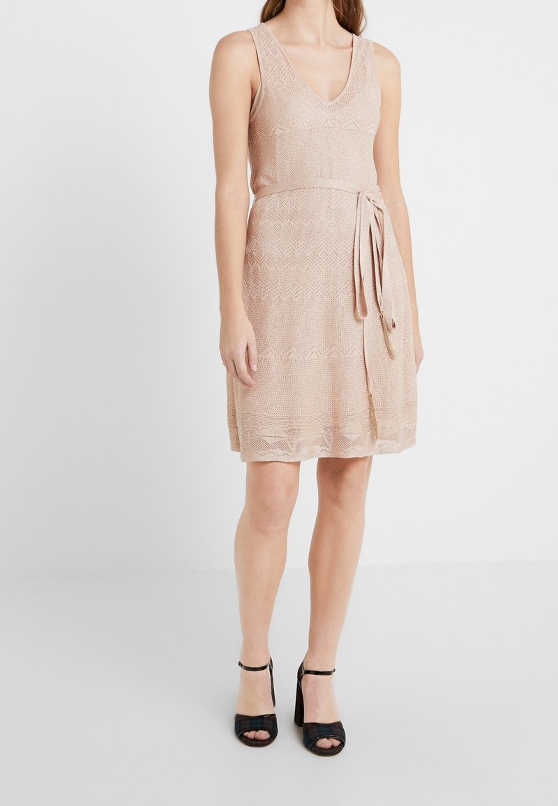 Une robe sans manches mi-longue en tricot pêche clair avec un motif texturé, un col en V et une taille cintrée avec une ceinture à nouer.