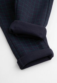 Granatowe spodnie w kratkę w kolorze turkusowym. Mają ściągacze przy mankietach i miękki, teksturowany materiał. Złożone na mankietach i starannie ułożone.