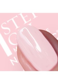 Glansig ljusrosa nagellack applicerat på en nagel, som visar en slät, glänsande finish med en subtil kurvig form. Bakgrunden innehåller varumärkeslogotyp.