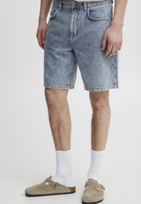 Denim shorts in light blue with a faded wash, four pockets, belt loops, and a straight-leg design. Paired with beige slip-on shoes.